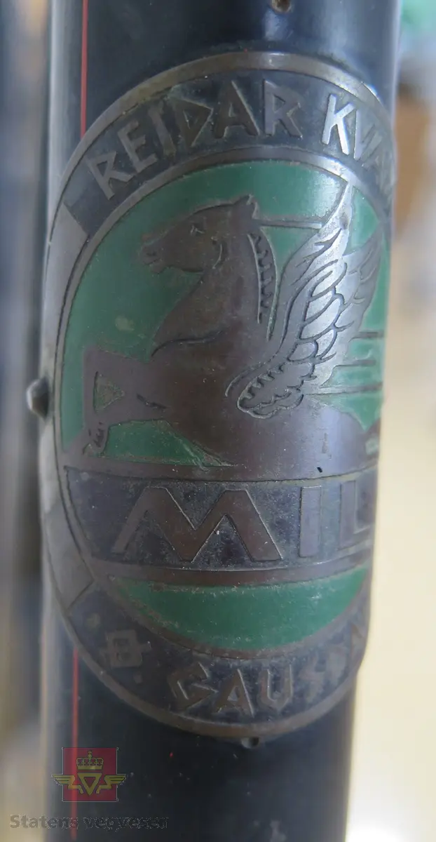 Tråsykkel, damemodell. Har to hjul, styre, sete, pedaler, frontlykt, ringeklokke, bagasjebrett, dynamo og refleks bak. Svart med rød staffering. Brunt sete og røde holker på styret. Sykkelen er i hovedsak lagd av metall, gummi og skinn.
Emblem med teksten: REIDAR KVAM Ø. GAUSDAL MIL.