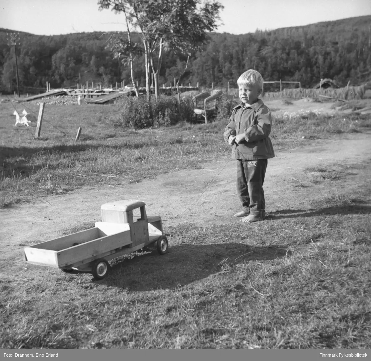 En lyslugget og barbeint Jarle Karikoski fotografert på et gårdstun  en sommerdag.