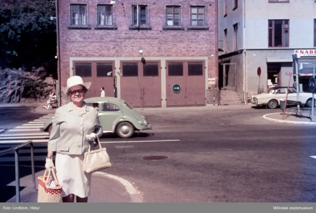En kvinna vid Gamla Torget i Mölndal, 1970-tal. I bakgrunden ses Kvarnbygatan 41, tidigare brandstation och garage för polisbilar, numera Mölndals målarskola. Till höger ses del av huset Kvarnbygatan 43, tidigare Mölndals stadshus, sedermera musikskola.

För mer information om bilden se under tilläggsinformation.