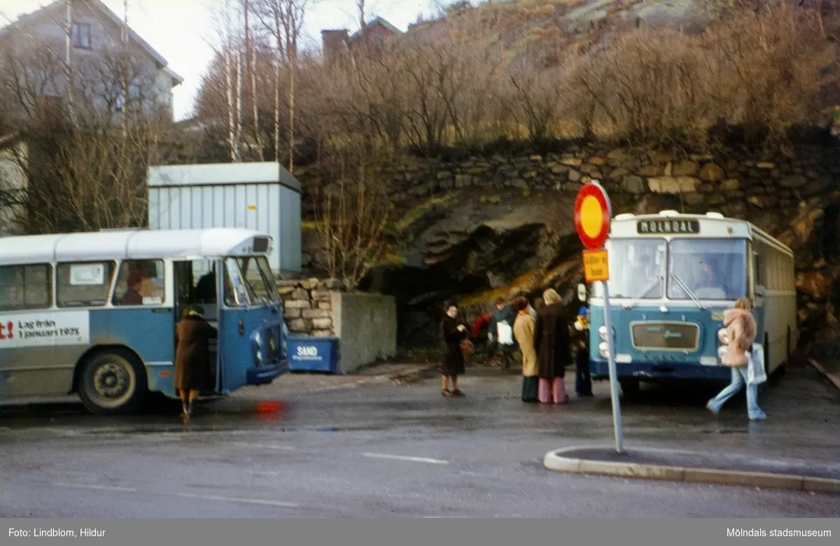 En samling människor står vid två blå bussar på en busshållplats vid Gamla Torget i Mölndal, 1970-tal.

För mer information om bilden se under tilläggsinformation.