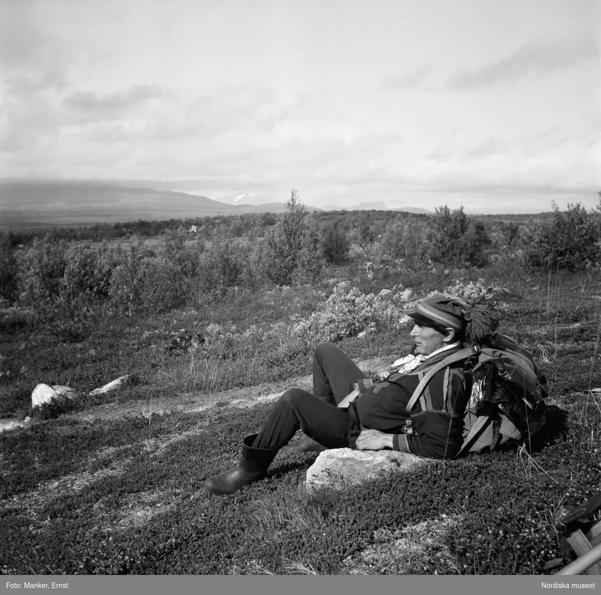 Utsikt från Kaivares sydsluttning västerut mot bl. a. Ripasasjaure. Olof Turi vilar i gräset iförd samisk dräkt. Nordiska museets Lappmarksinventering.