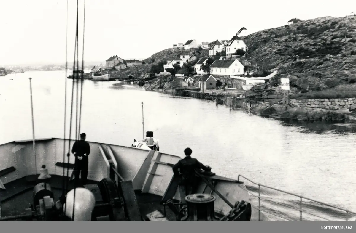 Kystbebyggelse i Norge tatt fra skip med baugen i forgrunnen.