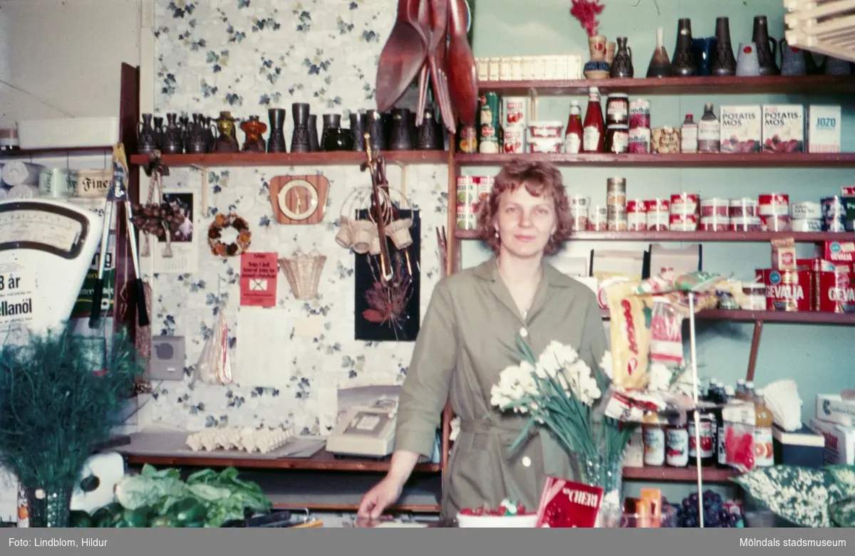 En kvinna står bakom disken i en speceriaffär, troligtvis vid eller i närheten av Gamla Torget i Mölndal, 1970-tal.

För mer information om bilden se under tilläggsinformation.