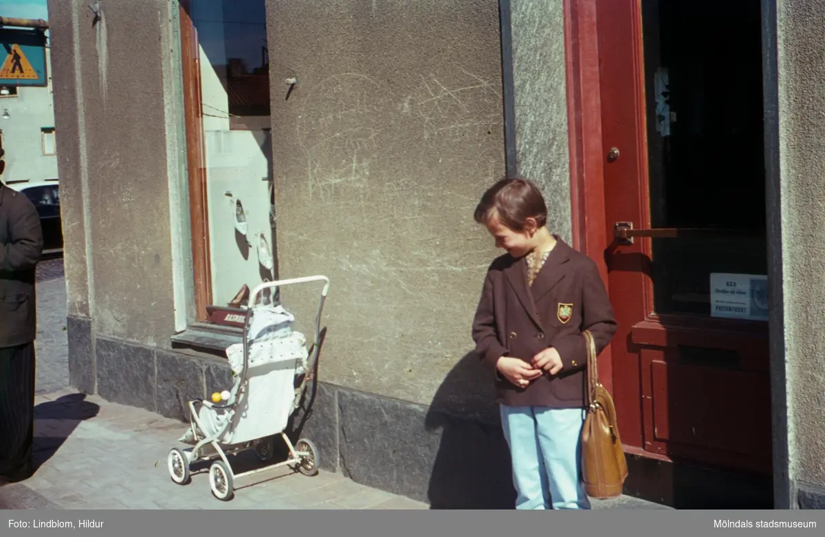Lisbeth Sjöberg, dotter till Märta Sjöberg, fotograferad på trottoaren utanför Rasmussons skoaffär med adress Kvarnbygatan 4 vid Gamla Torget i Mölndal, ca 1961-1962. På trottoaren står även en sulky.

För mer information om bilden se under tilläggsinformation.
