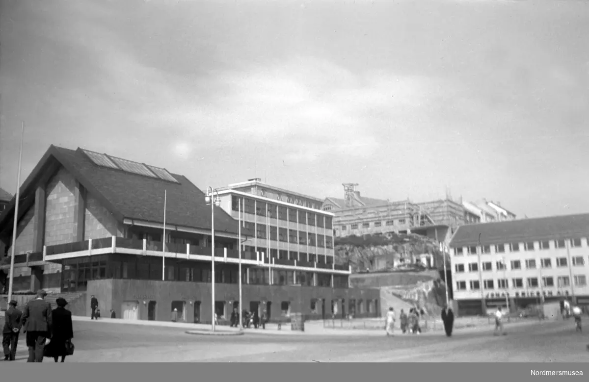 På bildet ser vi Kaibakken, Rådhuset (med adressen Kaibakken 2) og Rådhus-plassen (tidligere Fisketorget) fra venstre til midt på bildet. Ellers midt på bildet i bakgrunnen, ser vi Hotell Fosna under bygging, og til høyre ser vi Jonas Eriksens butikklokaler. Bildet er datert Juni 1953. Nordmøre Museums fotosamling 
