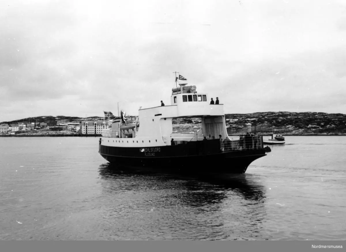 Bildet viser B/F"Norddalsfjord" Storviks Mek. Verksteds bnr.14 som legger fra kai ved verkstedet for å gå på teknisk prøvetur. Vi ser at verkstedsflagget og det norske flagget er heist.

"Norddalsfjord" ble levert til Møre og Romsdal Fylkesbåtar 15. mars 1961 og hadde følgende hoveddimensjoner: L 31,20 m x B 8,55 m x D 3,35 m og hadde en tonnasje på 159 bruttoregistertonn. Fremdriftsmaskineriet består av 3 Volvo Penta turboladede dieselmotorer type TMD96 på til sammen 420 hk som via kilremdrift var koblet til et felles gir og propellaksel med vribar propell, slik at hver enkelt av motorene kunne kjøres separat. Fergen hadde 2 Bolinders vekselstrømsaggregater type 1052MG på 23 hk hver tilkoblet en generator på 17 kW. Fergen var utstyrt med elektrohydraulisk styremaskin.

Fergen har plass til 18 personbiler og har sertifikat for 160 passasjerer. Forut er det innredet 6 lugarer for offiserer og restaurantpersonale og akterut en mannskapslugar for 4 personer og toppfarten er 11,4 knop og marsjfarten 10,5 knop.

Ferga er verkstedets første nybygg etter B/F"Trygge" som ble levert i 1938.

Personene på dekk og på brua er vanskelige å kjenne igjen, men personen til venstre på dekket bak bilporten er adm. direktør Bjørn Bugge i Møre og Romsdal Fylkesbåtar. Personen i midten på høyre side bak bilporten, med hvitt skjerf, er verkstedets driftsleder Anders Voldnes.

I bakgrunnen ses en motorskøyte og Skorpa med Visnesbrygga.

Bildet er fra 1961. Kilde/tekst: Peter Storvik. Fra Nordmøre museums fotosamlinger.
