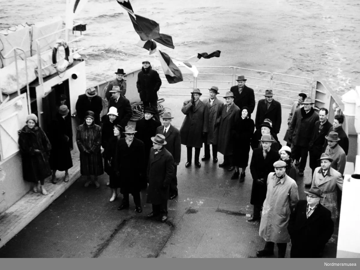 Bildet viser bakre bildekk på B/F”Norddalsfjord” Storviks Mek. Verksteds bnr.14 på overleveringsturen og ved flaggskiftet på Bolgsvaet ved Kristiansund. Mange personer er samlet på dekk.
”Norddalsfjord” ble levert til Møre og Romsdal Fylkesbåtar 15. mars 1961 og hadde følgende hoveddimensjoner: L 31,20 m x B 8,55 m x D 3,35 m og hadde en tonnasje på 159 bruttoregistertonn. Fremdriftsmaskineriet består av 3 Volvo Penta turboladede dieselmotorer type TMD96 på til sammen 420 hk som via kilremdrift var koblet til et felles gir og propellaksel med vribar propell, slik at hver enkelt av motorene kunne kjøres separat. Fergen hadde 2 Bolinders vekselstrømsaggregater type 1052MG på 23 hk hver tilkoblet en generator på 17 kW. Fergen var utstyrt med elektrohydraulisk styremaskin.
Fergen har plass til 18 personbiler og har sertifikat for 160 passasjerer. Forut er det innredet 6 lugarer for offiserer og restaurantpersonale og akterut en mannskapslugar for 4 personer og toppfarten er 11,4 knop og marsjfarten 10,5 knop.
Ferga er verkstedets første nybygg etter B/F”Trygge” som ble levert i 1938.
Bildet er fra 1961.
Bildet viser personene som var med på overleveringsturen med B/F"Norddalsfjord".
Fra venstre, forrest: ukjent, Agnes Gaupseth Storvik, Berit Storvik, ukjent, Inger Otelie Storvik, Lars Mogstad Storvik, banksjef Haugan.
Rekke to fra venstre: ukjent, Christian Larsen, Paul Storvik, ukjent.
De to i rekke tre fra venstre: skipskontrollør Bonsak  og Jørgen Wirum.
Forreste rekke til høyre fra venstre: ukjent, ukjent fra MRF, ukjent, Andrea Storvik Dørge, 
gudmoren fru ordfører Olav Aarø,  muligens ordfører i Vanylven Olav Aarø, Harald Svendsen, ukjent, Anders Voldnes, ukjent.
Bakerste rekke til høyre fra venstre: Egil Olsen, Ivar Kjærvik, Bjørn Arntsen, Martin Strømsvåg, Per Strand, Peter Andreas Storvik, Olaf Gaupseth, ukjent. ----
Bildet viser bakre bildekk på B/F"Norddalsfjord" Storviks Mek. Verksteds bnr.14 på overleveringsturen og ved flaggskiftet på Bolgsvaet. Mange personer er samlet på dekk.

"Norddalsfjord" ble levert til Møre og Romsdal Fylkesbåtar 15. mars 1961 og hadde følgende hoveddimensjoner: L 31,20 m x B 8,55 m x D 3,35 m og hadde en tonnasje på 159 bruttoregistertonn. Fremdriftsmaskineriet består av 3 Volvo Penta turboladede dieselmotorer type TMD96 på til sammen 420 hk som via kilremdrift var koblet til et felles gir og propellaksel med vribar propell, slik at hver enkelt av motorene kunne kjøres separat. Fergen hadde 2 Bolinders vekselstrømsaggregater type 1052MG på 23 hk hver tilkoblet en generator på 17 kW. Fergen var utstyrt med elektrohydraulisk styremaskin.

Fergen har plass til 18 personbiler og har sertifikat for 160 passasjerer. Forut er det innredet 6 lugarer for offiserer og restaurantpersonale og akterut en mannskapslugar for 4 personer og toppfarten er 11,4 knop og marsjfarten 10,5 knop.

Ferga er verkstedets første nybygg etter B/F"Trygge" som ble levert i 1938.

Bildet er fra 1961. Kilde/tekst: Peter Storvik. Fra Nordmøre museums fotosamlinger.












 Tilleggsopplysning: Bildet er fra overleveringsturen til B/F";Norddalsfjord"; bnr. 14 fra Storviks Mek. Verksted til Møre og Romsdals Fylkesbåtar og viser noen av personene som var med på overleveringsturen.



















 (Informant:
 Peter Storvik.)