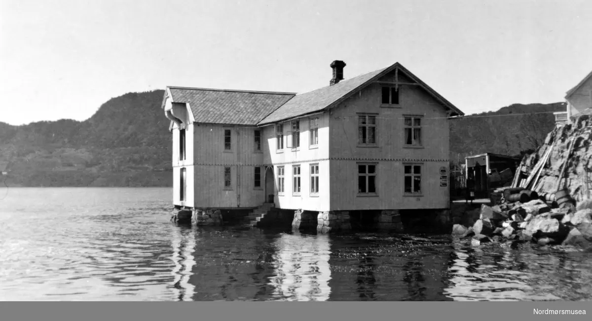 Foto av en brygge liggende helt nede ved sjøkanten usikkert hvor, Aure? Trapp ned i sjøen, kolonial, skilt, dampskipsstoppested, handelssted? Datering er også usikker, men sannsynligvis omkring 1920 til 1939.
Fra Nordmøre museums fotosamlinger.
