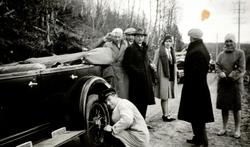 Foto av en gruppe menn og kvinner samlet ved en bil stående 