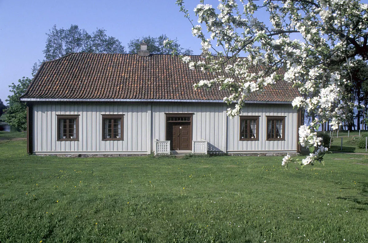 Hvitt trehus med valmet tak og blomstrende epletregren i forgrunnen.