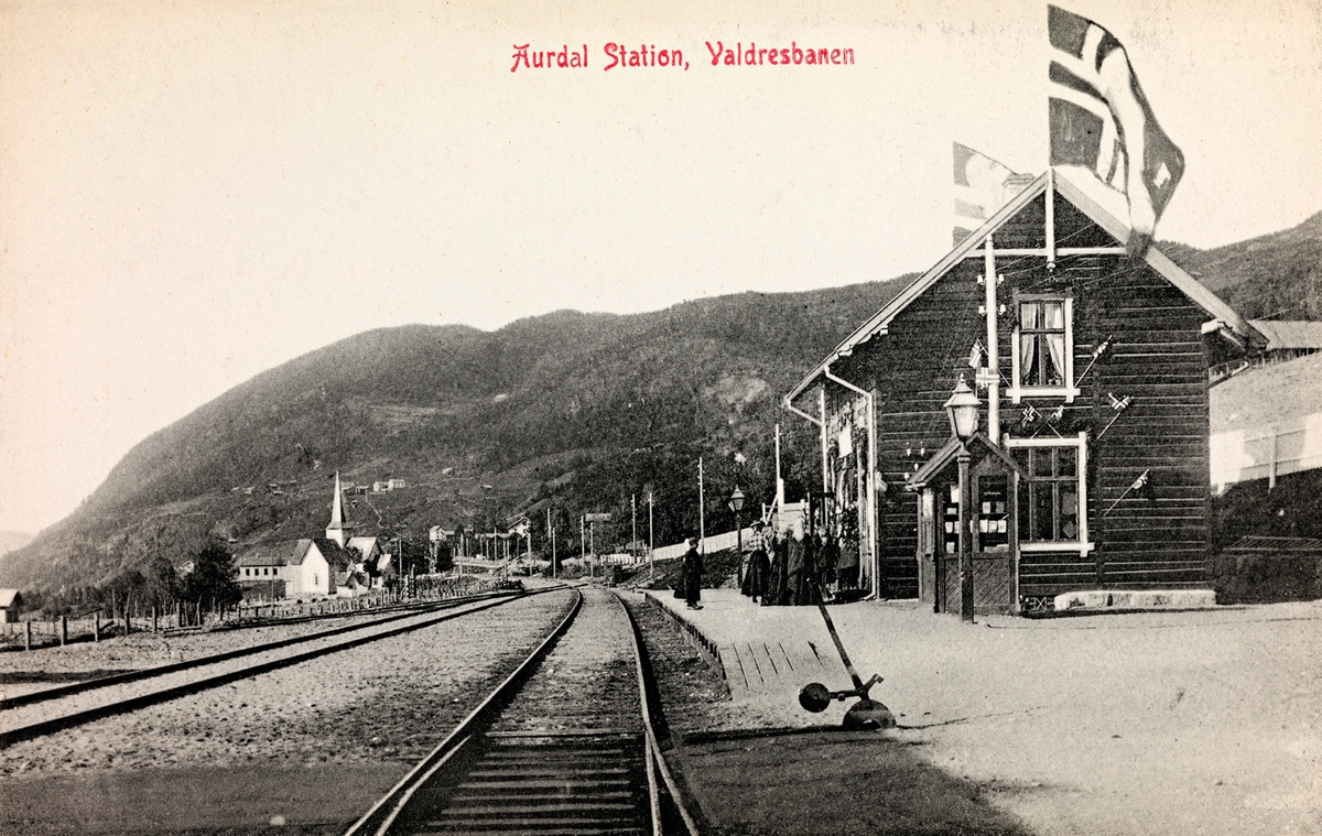 Aurdal jernbanestasjon, trolig fotografert i forbindelse med åpningen av Valdresbanen Dokka-Fagernes. Stasjonen er pyntet med flagg.
