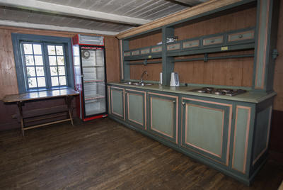 Barfrøstua har eget kjøkken med oppvaskbenk og kokeplater. Gammelrosa malte vegger og grønnmalt innredning.