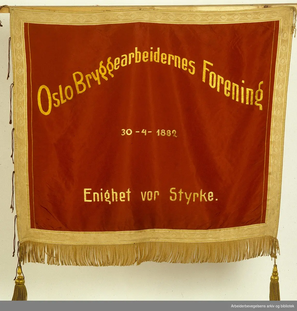 Oslo bryggearbeideres forening.stiftet 30. april 1882..Forside..Fanetekst: Oslo Bryggearbeidernes forening.30 - 4 - 1882. .Enighet vor Styrke...