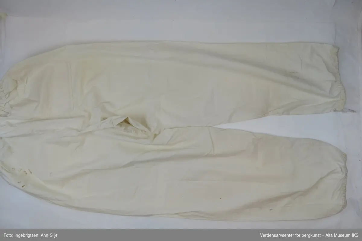 Hvit tøybukse med strikk i linningen og nederst på buksebena. Baklomme på høyre side.