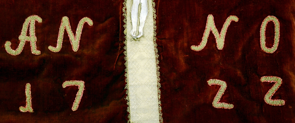 Kristus figur med armene opp i sølvrelieff. Montert på kors av silkebånd.