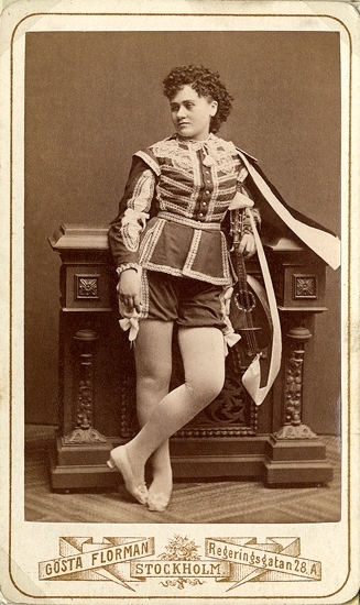 Rollporträtt (helfigur) av operasångerskan Carolina Östberg i mansdräkt med cape.