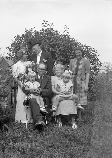 Foto av ett brudpar med familj, fotograferade i en trädgård.