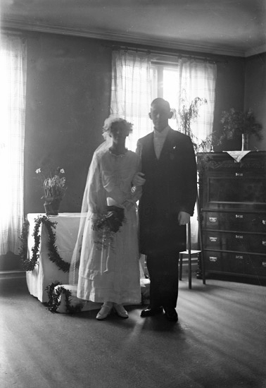 Bröllopet i Ärla (Ärila) 31 mars 1918 mellan bruksbokhållaren Fritz Bergqvist (1890-1957) och Agda Fors (1888-1964).  
En man och kvinna i bröllopskläder står framför ett bord arrangerat som altare.
I bakgrunden syns lite blommor och en byrå. 
                                                          .