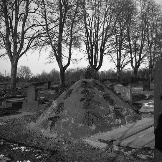 En granrisdekorerad jordhög intill en nyss uppgrävd grav på kyrkogård. Göteryd.