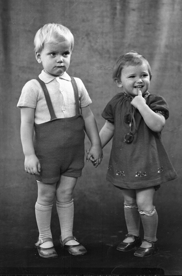 Foto av två små barn, en pojke och en liten flicka. Syskon (?). 
Helfigur. Ateljéfoto.