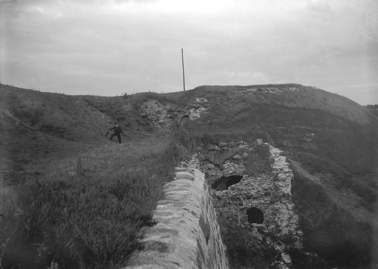 Foto av de gräsbevuxna fästningsvallarna. I bakgrunden syns en man med hatt.