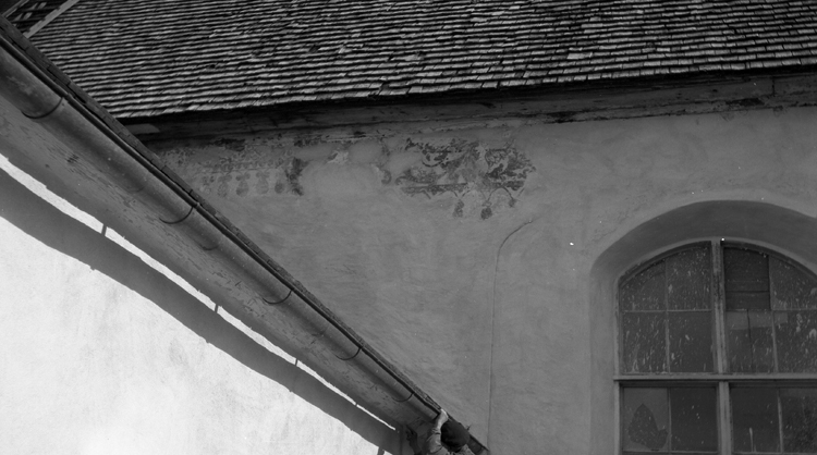 Foto på en kyrka med ett fönster, med rester av kalkmålning på ytterväggen.