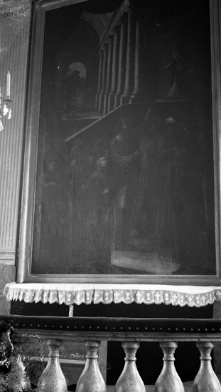 Foto på en altarmålning, framför står altarbordet och altarrundeln.