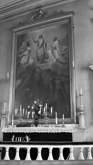 Närbild på altarmålningen. nedanför står altarbordet med ljusstakar på och altarrundeln utanför.