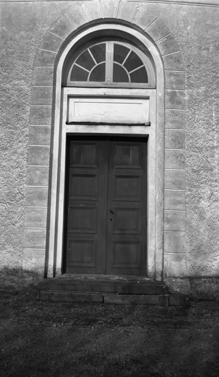 Foto på en kyrka med närbild på dörren med ett fönster ovanpå.