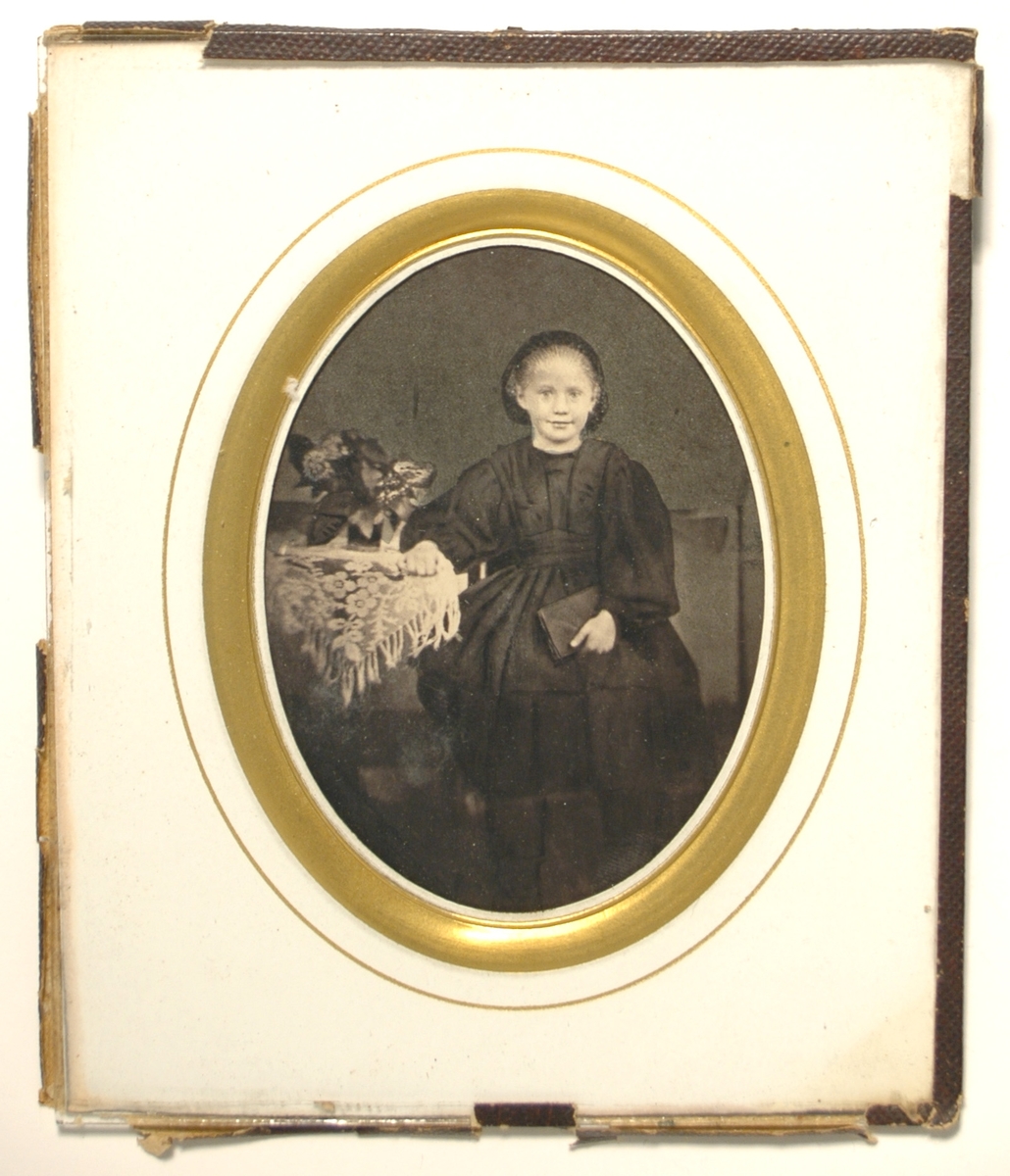 Fotografi på papper monterat med klotkant bakom glas, oval form. Vit kartong med förgylld kant och guldlinje.