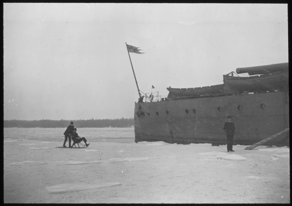 Svenska militärer åker sparkstötting på isen nedanför aktern på pansarskeppet SVERIGE under Ålandsexpeditionen 1918