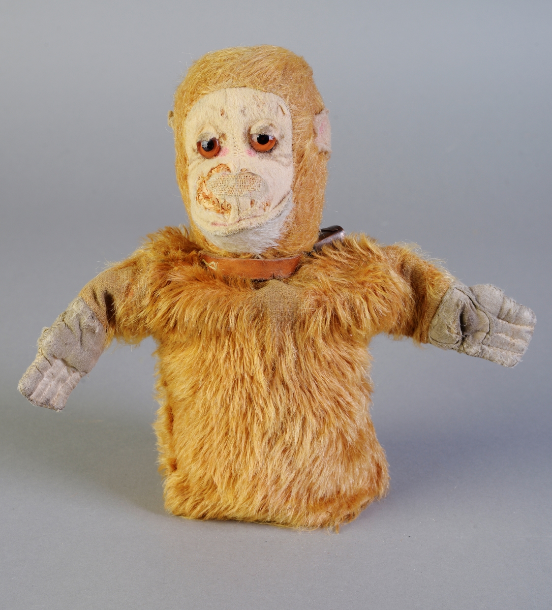 En fingerdukke som er en apekatt som er laget av brunoransje kunstpels. Hendene er laget av bomullsstoff, mens ansiktet og ørene er laget av filt. Øynene er laget av glass. Hodet er fylt med trespon. Den er ganske slitt og er ødelagt i ansiktet. Rundt halsen har den en skinnreim med bjelle på. Denne ble satt på senere (pers. med.), og det er antageligvis en souvenir som er brukt (siden det står "Rena" på bjellen.