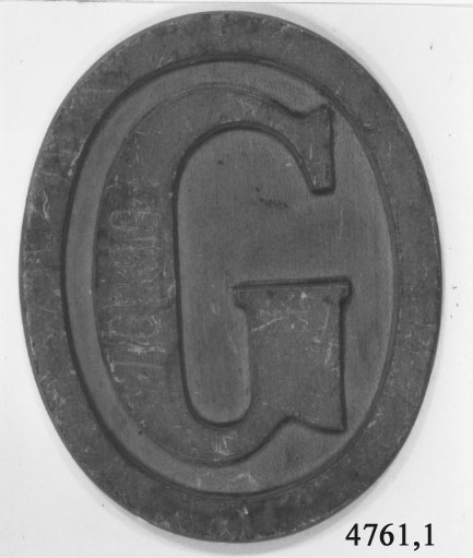 Stävmärke, modell. Av trä. Utgör en oval, gulmålad bricka med bokstaven G.
Märkt på framsidan: 6339,7 och på baksidan med bläck: 2 st. av mässing till Götas Båtar.