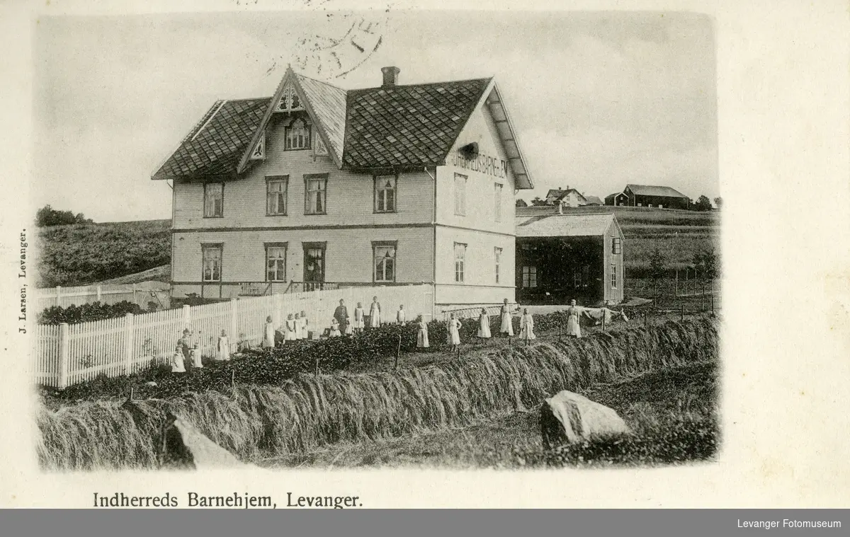 Postkort av barrnehjemmet på Levanger, barna foran bygningen i grønnsakfeltet.
