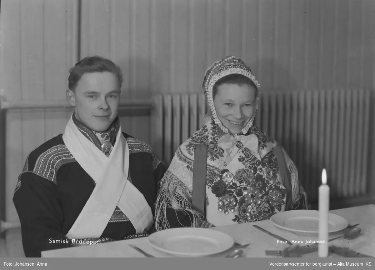Samisk brudepar som sitter til bords. Hvit duk, hvitt lys.