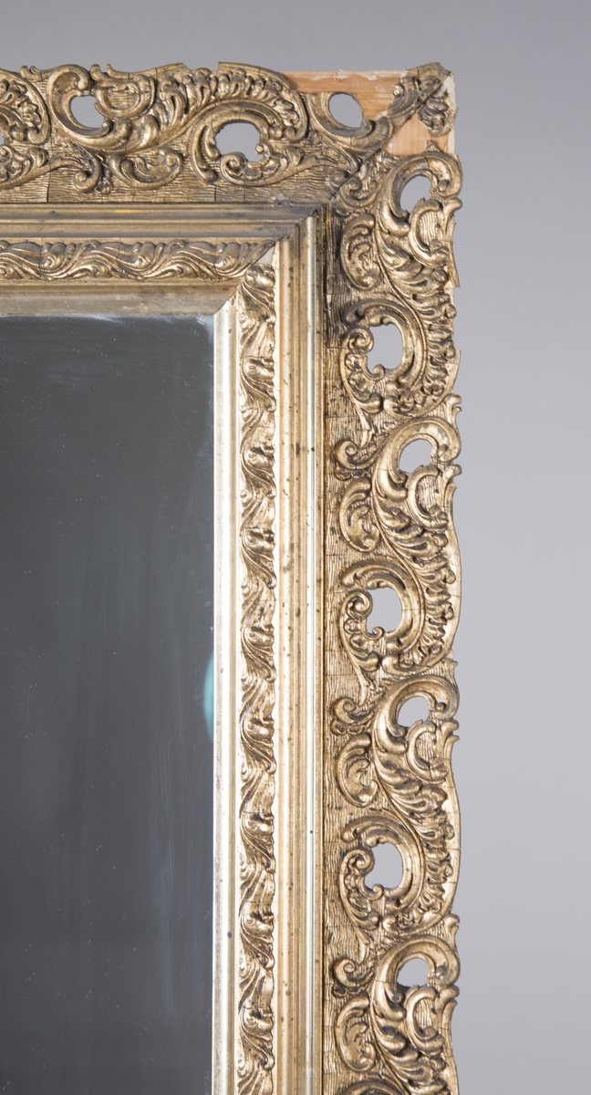 Rektangulært speil med forgylt ramme. Opphøyd rammekant inntil speilet, med asymmterisk ornament rundt dette. Støpt ornament som er limt på treverk.