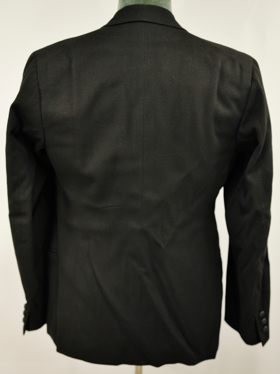 A: Jakke, Svart klede, krage med silkeslag. Enkeltspent, 1 trekt knapp, 3 trekte knapper på kvar arm. Svart silkefor. L.71,5 cm bredde ved skuldrane 45 cm
B: Bukse, svart klede, silkeripsbånd i sidene. L. 103 cm, Vidde nede 24 cm
C: Vest, svart klede, svart silkefor i rygg, foret med lystripet sateng. Enkeltspent med 4 trekte knapper, 4 lommer. L.48,5 cm x 38 cm
D: Sløyfe, Sort silkerips 55cm x 3,5 cm