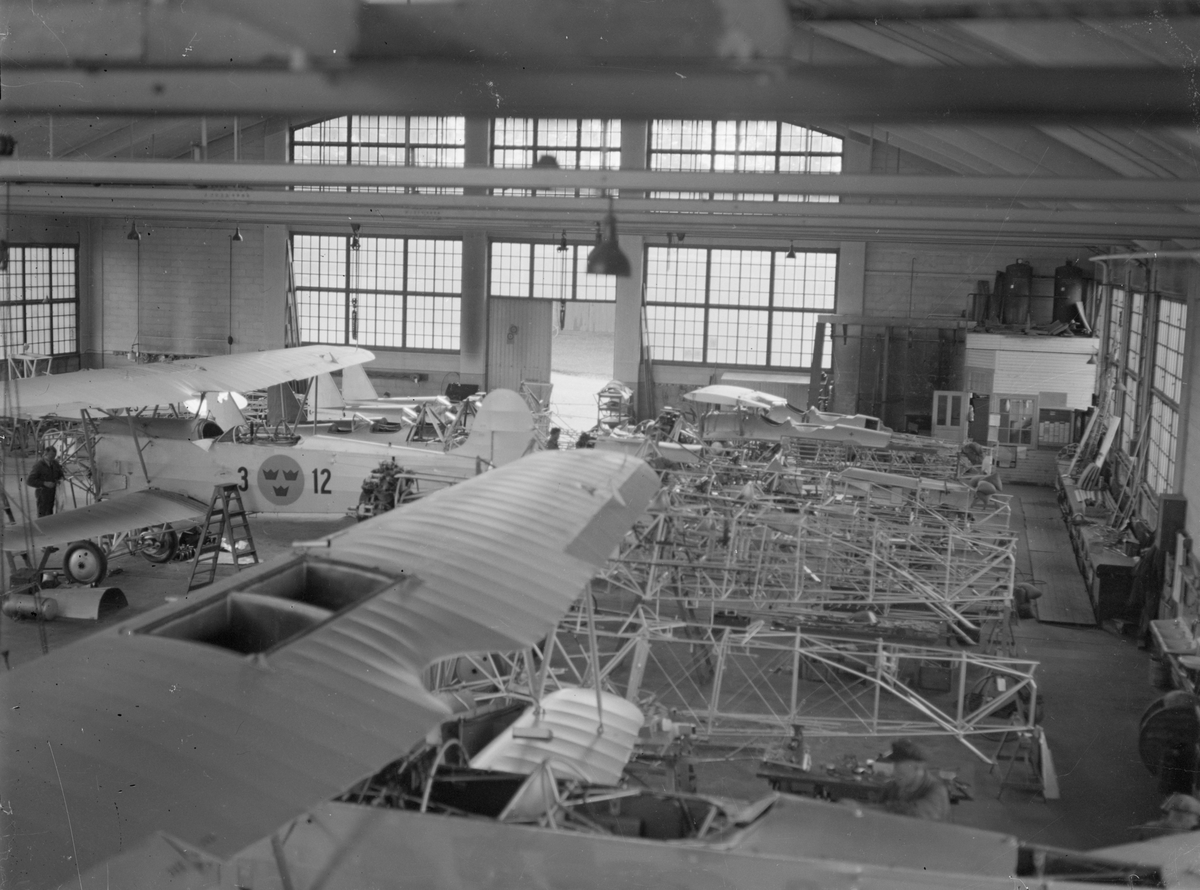 Montering av Fokker-flygplan i hangar på Centrala verkstaden Malmslätt. Till vänster syns en man arbete med flygplan S 6 märkt 3-12.