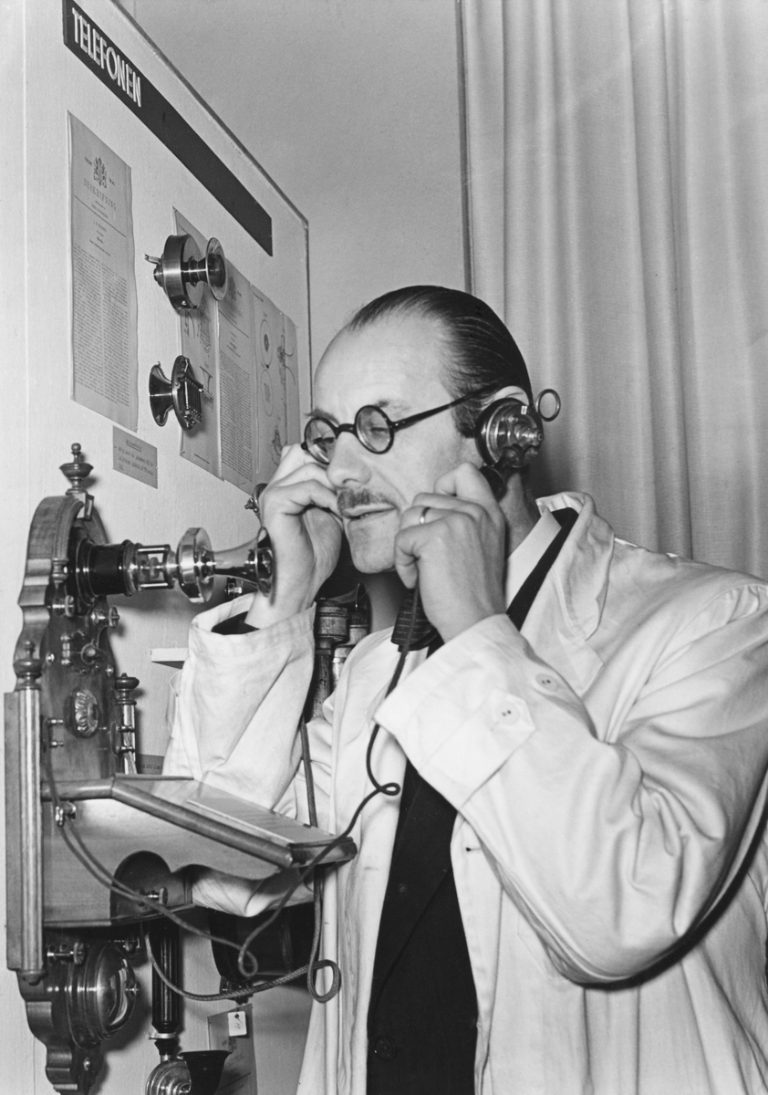 Museidirektör Torsten Althin demonstrerar en av L.M. Ericssons första väggtelefonapparater vid öppnandet av utställningen Idé- Patent- Produkt, på Tekniska museet den 6 december 1941.