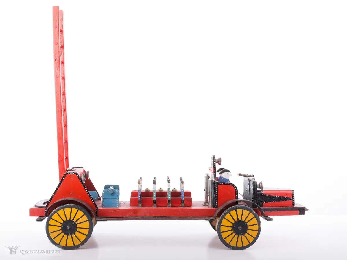 Hjemmesnekret leke- brannbil i tre og stål med med bevegelige hjul og stige med sveivemekanisme.. Modeller av to brannmenn i et åpent førerhus, og åtte brannmenn sitter på en benk på lasteplanet.