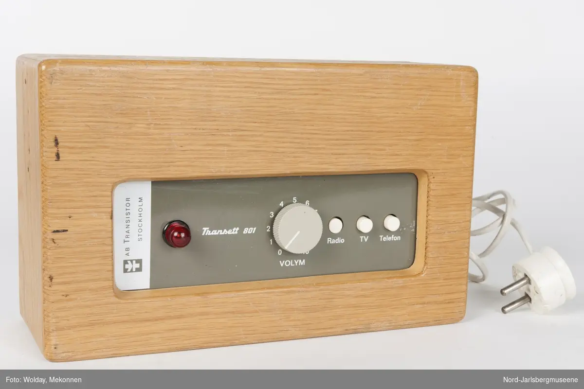 Firkantet apparat, som en liten radio. kassen er bygget av tre.
dsen kan kobles til telefon og radio, TV, eller brukes i forsamling med høreapparat. Antatt fra tidlig 1970-tall.