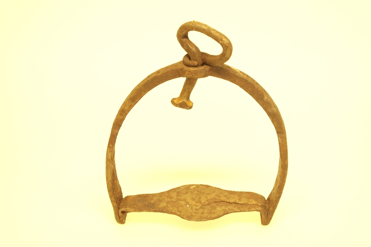 Hesteskoformet stigbøyle i smidd jern. Bøylen er bredere mot fotplaten. Fotplaten er bredest midt på ornamentert med prikker.