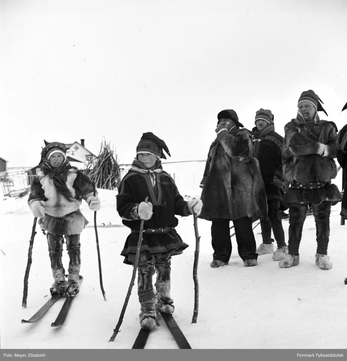 Unger på ski i Kautokeino. I bakgrunnen står Mikkel Mikkelsen Logje og Isaac Johansen Hætta m.flere.