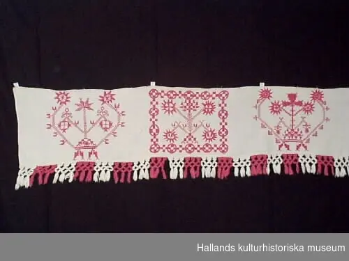 Hängkläde av linne med röda hallandssömsbroderier. Vita bomullsband i form av hällor är fastsydda i överkanten. Märkning, broderat: "EBBD", "1853". Frans +:70 mm. 