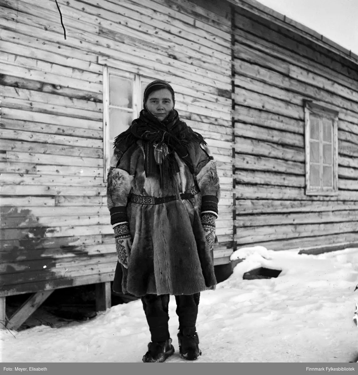 Ellen Johnsdatter Utsi kledd i samisk pesk med samisk belte, lue, sjal og votter. Fotografert av Elisabeth Meyer, mulighens i perioden rundt påske 1940 i området Kautokeino.