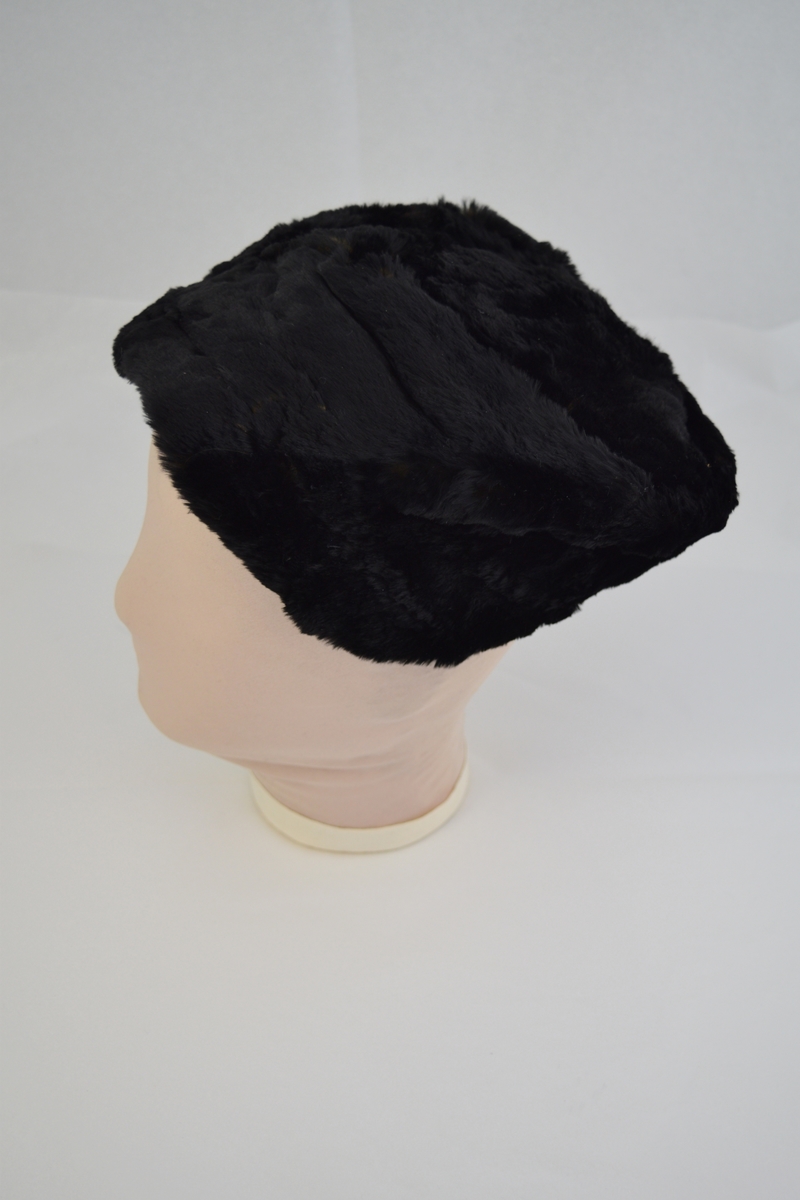 Hatt av pels med for i tynt blankt stoff. Hatten har en devis rund form og består av en rund topp med en bred kant.