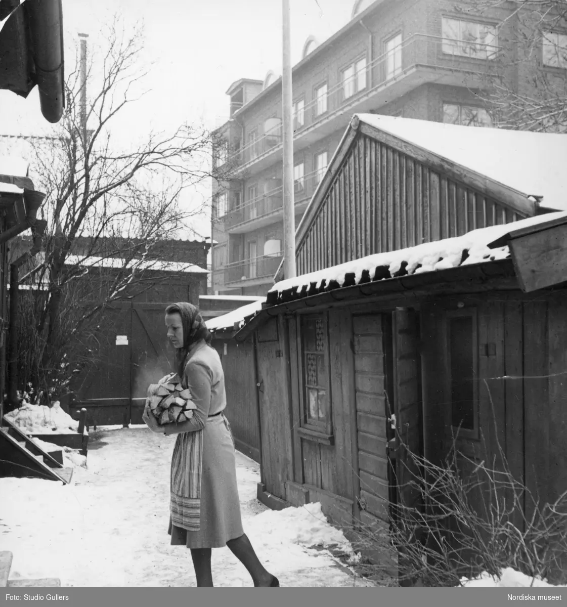 Fru Birgitta Törnqvist bär ved på en bakgård på Mäster Mikaels gata 9, Södermalm, Stockholm.