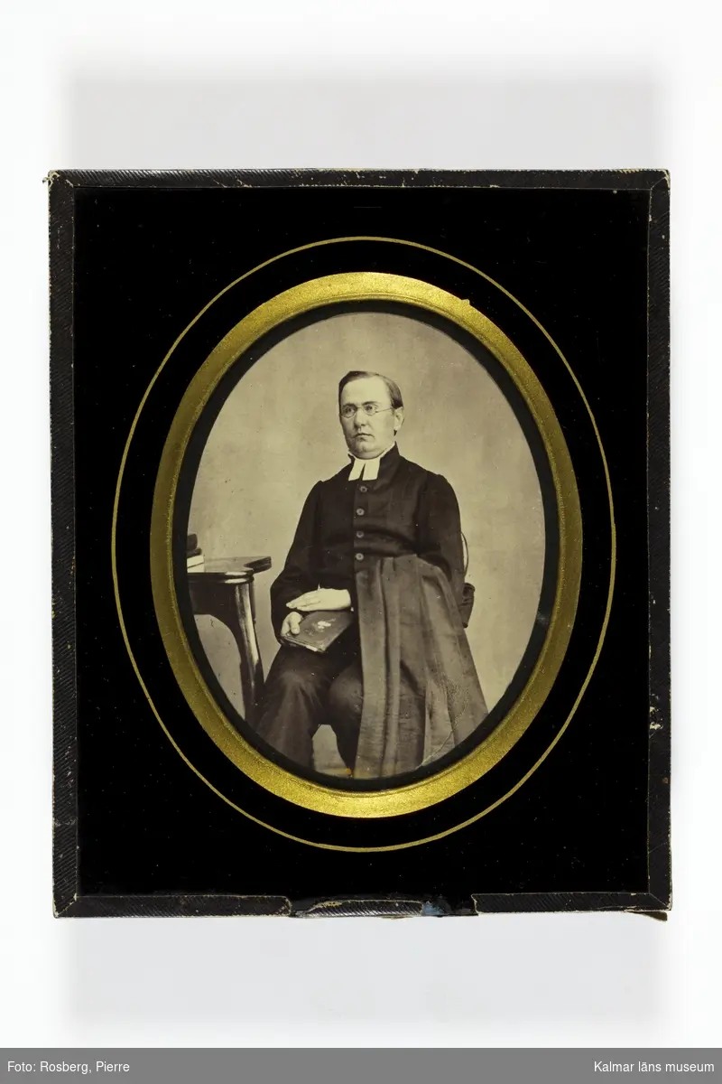 Porträtt av P G E Stark, kyrkoherde, med prästklädsel, sittande med kappan över vänster arm och en bok i höger hand.