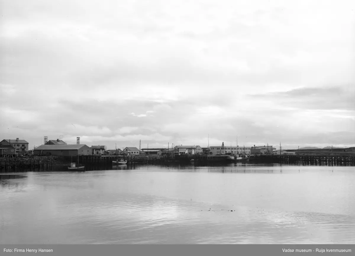 Bildet viser Vadsø havn sett fra vest 16.09.1951. I venstre halvdel ser en to fiskebåter. Litt til venstre for midten av bildet ser en bensinstasjonen til Norsk Brændselolje. Til høyre i bildet ser en havneterminalen med det flate taket.  Framfor dampskipsbygget ses en mast som anses være et fortøyningsanlegg for sjøflyene som landet på havna. Helt til høyre ser en dampskipskaia.