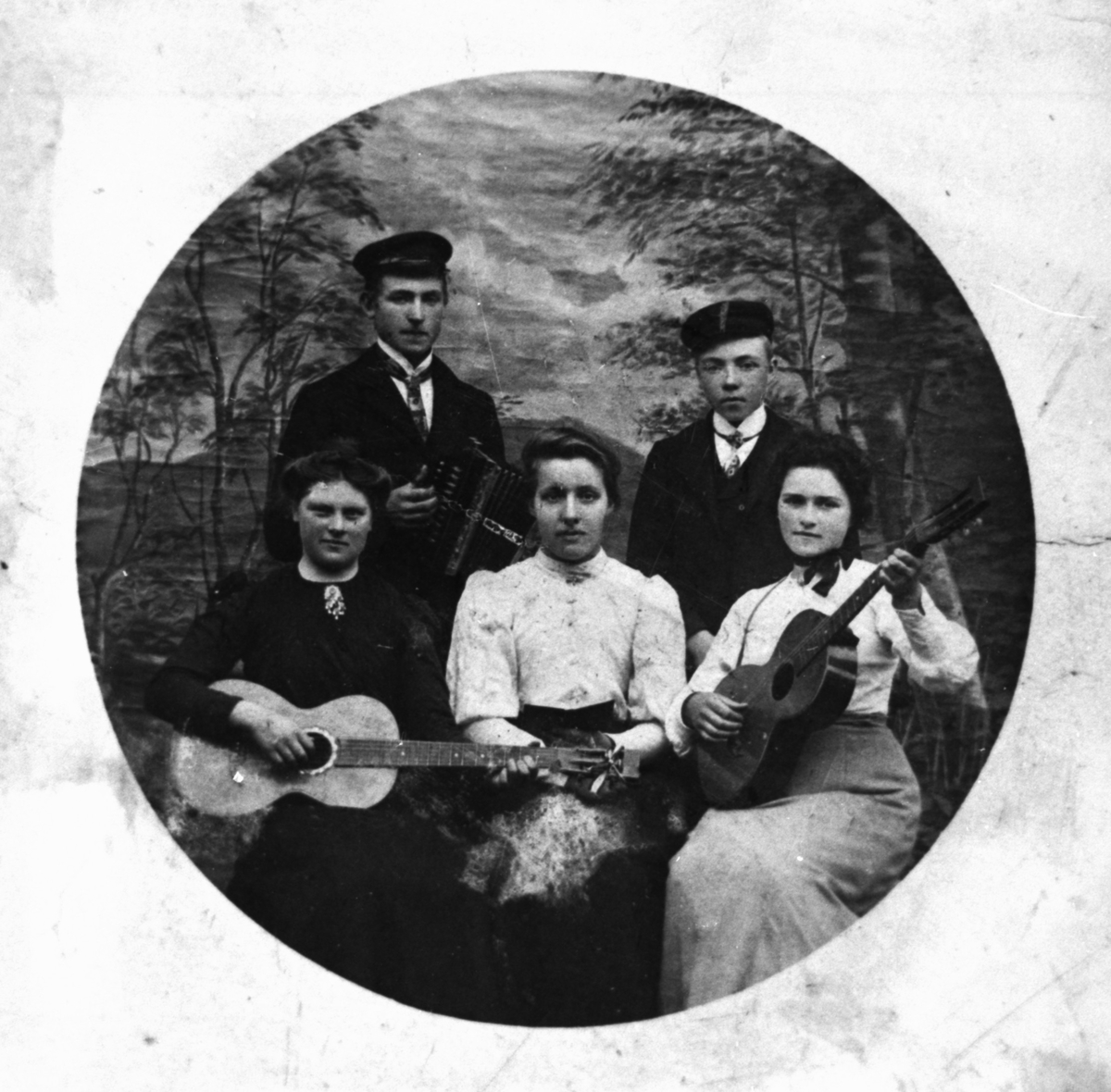 Gruppeportrett i fotostudio av fem personer. To har gitar i hendene, en har trekkspill.